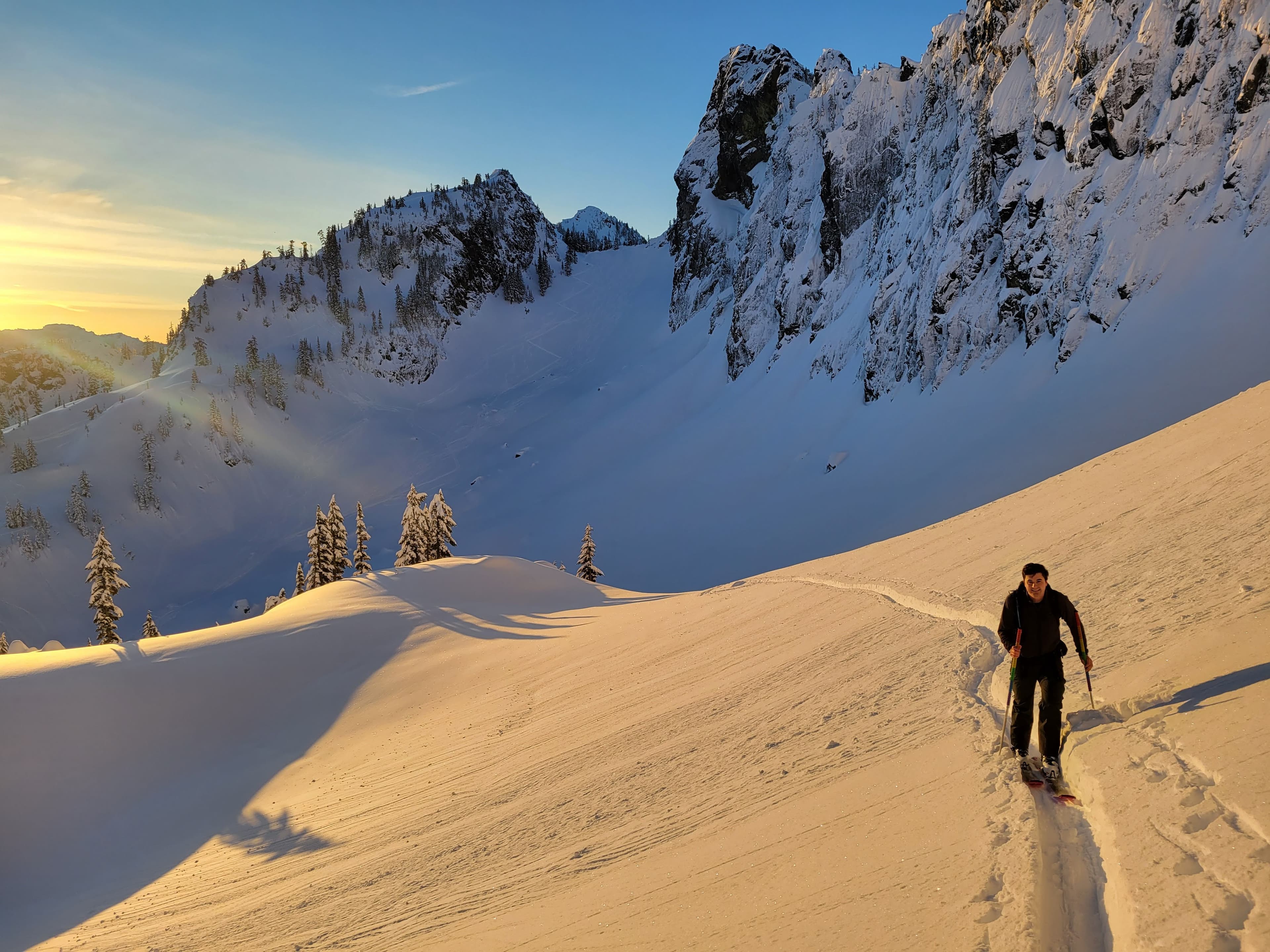 Early morning light on a snowy ridge, with the long shadows of two skiers across the slope
