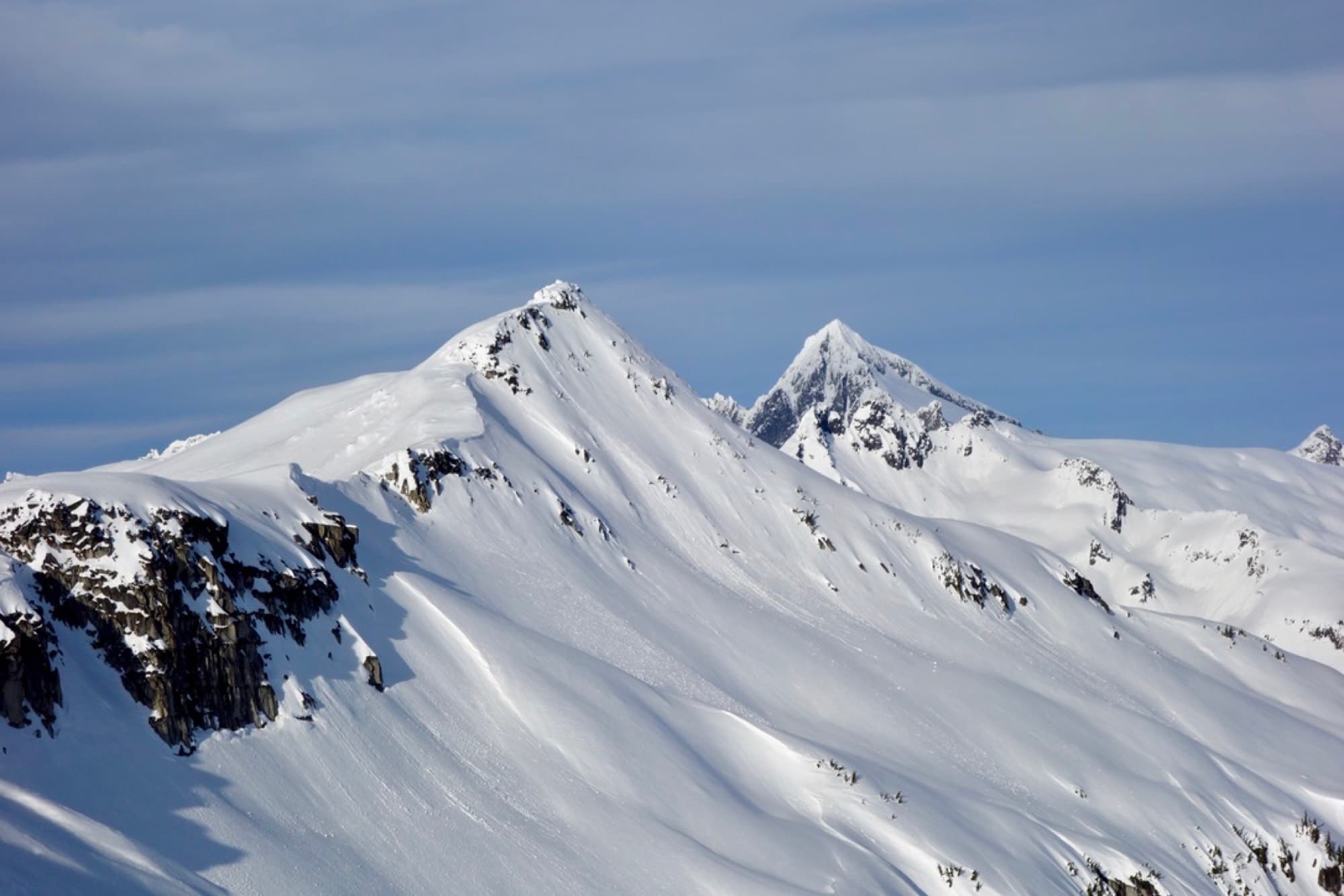 Two snow-covered Cascade peaks and a broad wind-sculpted ridge under blue sky